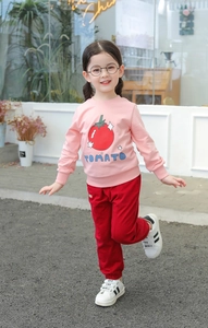 Outdoor shot of a toddler girl in a pink tomato sweatshirt and red joggers with sneakers
