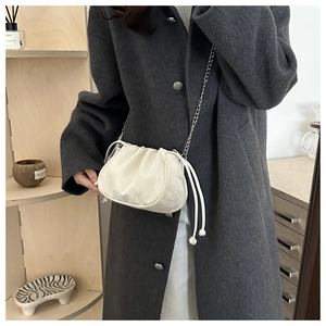 Detail of white ruched cloud bag featuring silver chain strap on grey wool coat