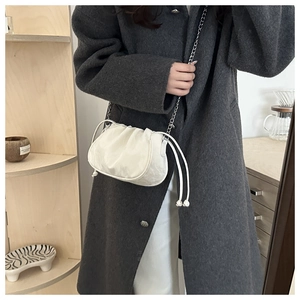 Close-up of white ruched bucket bag with silver chain strap shown on a model