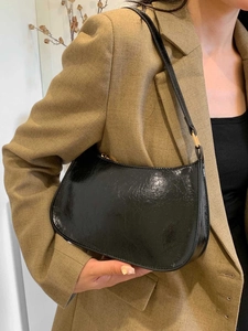 Sac hobo noir brillant pour femme porté avec un blazer kaki sur un fond blanc épuré