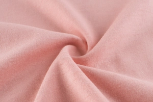 Close-up of soft pink knitted cotton fabric texture with spiral fold detailing