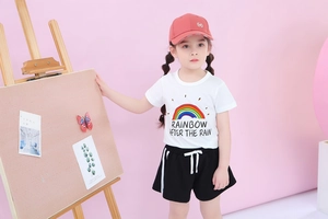 Girl's summer outfit featuring rainbow print T-shirt, black side-stripe shorts, and red cap