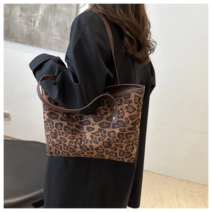 Détail du sac cabas léopard avec anses en cuir marron et écusson de marque sur toile