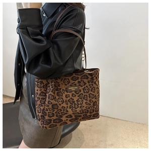 Detailed view of leopard print tote bag with metal brand plaque and dark brown handles