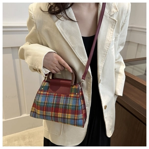 Détail d'un sac à main vintage à carreaux avec poignée en bois porté par un modèle