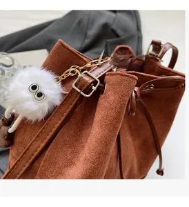 Close-up of brown suede bucket bag with gold hardware and white plush monster charm