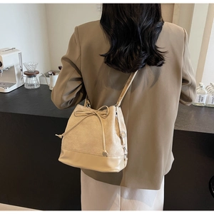 Detailed view of beige bucket bag featuring bow drawstring and leather texture on a model