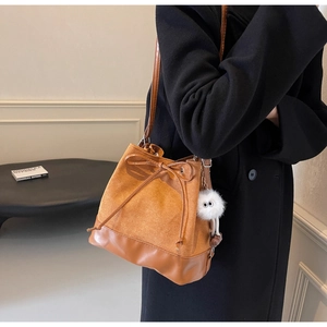 Detail of a brown bucket bag showing suede texture, drawstring bow, and plush charm