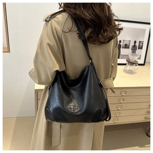Detail of black matte leather tote bag with wide strap and embossed fashion logo