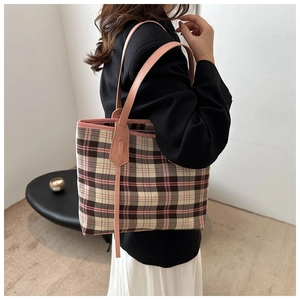Detail of a large plaid tote bag with pink leather straps worn with a black blazer