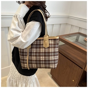 Close-up of a checkered tote bag with leather trim worn by a model in a minimal setting