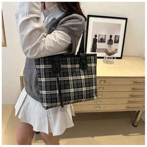 Detail of grey plaid canvas tote bag with black leather straps and decorative ribbons