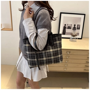 Detailed view of large plaid tote bag worn by model in a warm minimalist interior setting