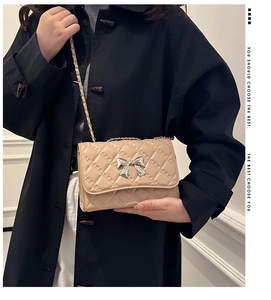 Quilted beige crossbody bag featuring a silver bow buckle and leather chain strap detail