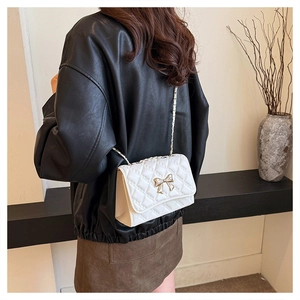 Close-up of white quilted crossbody bag with gold bow on a woman in a black leather jacket