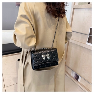 Detail of black quilted chain bag with silver bow ornament worn with beige coat