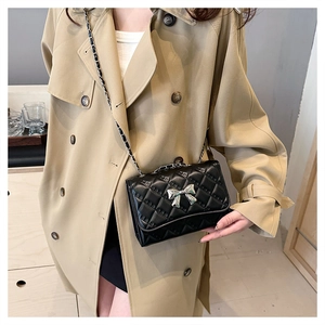 Close-up of black quilted crossbody bag with silver bow accent on a trench coat