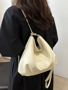 Cream white leather tote bag in minimalist hobo style worn by model over black coat