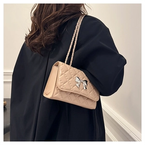 Beige quilted chain crossbody bag with silver bow charm shown on a female model