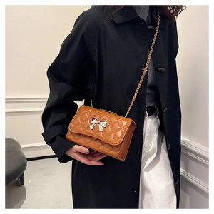Detail of a brown quilted crossbody bag featuring a silver bow-knot metal clasp and chain strap