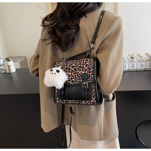 Leopard print backpack with plush charm worn by model in a stylish cafe setting