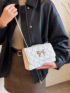 White quilted crossbody bag with silver bow accent and chain strap worn by a model