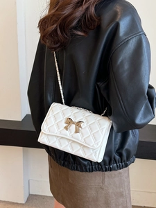 White quilted crossbody bag with gold bow clasp and chain strap on a model wearing black leather