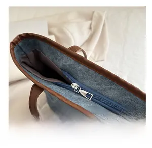 Dettaglio borsa tote in denim blu con finiture in pelle marrone e zip in metallo argento