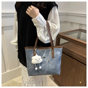 Minimalist denim tote bag with brown straps and plush smiley charm on white background