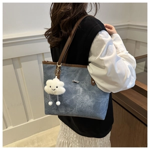 Detail of blue denim tote bag with brown leather trim and cute plush cloud keychain