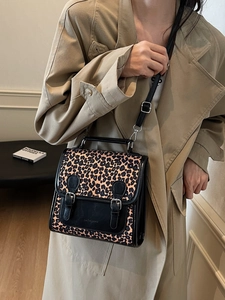 Chic leopard print crossbody bag with black buckle straps worn with a beige trench coat