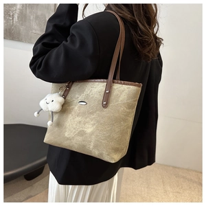 Detail of olive green tote bag with brown leather handles and a white cloud plush charm