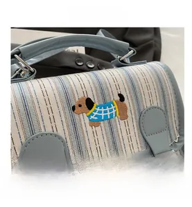 Detail of light blue bag with striped flap and dachshund embroidery on textured fabric