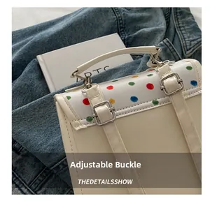 Detail of colorful polka dot flap and silver adjustable buckles on creamy leather bag
