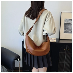 Detail view of large brown leather crescent bag with eyelet strap on model