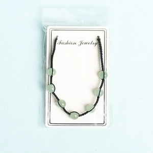 Handmade woven bead bracelet with green gemstones and black cord on jewelry card