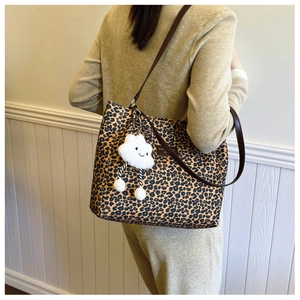 Detail of leopard print tote bag with brown leather straps and white plush pendant charm