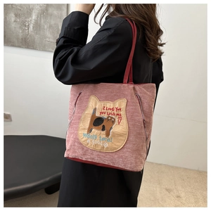 Detail of pink corduroy tote bag with cat embroidery and red strap on a model's shoulder