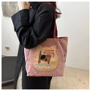 Detail of pink corduroy tote bag with cartoon cat patch and red shoulder straps