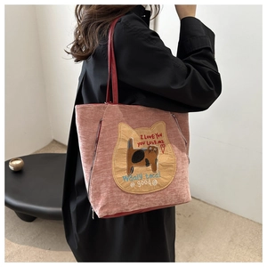 Detail of pink corduroy tote bag with cat embroidery and red shoulder strap on a model