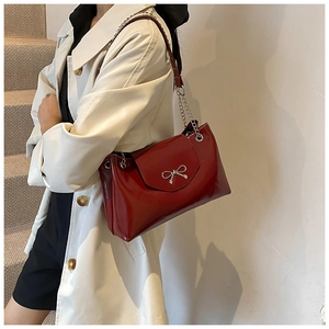 Détail du sac à bandoulière en cuir verni rouge avec nœud argenté et chaîne