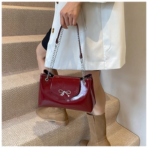 Macro shot of a wine red glossy patent leather tote bag with silver bow accent and chain strap