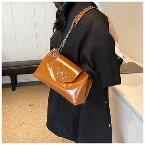 Sac fourre-tout en cuir verni marron avec boucle en métal porté par un mannequin en studio