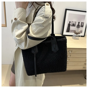 Dettaglio della borsa tote nera in pile con manici in pelle indossata su un trench beige