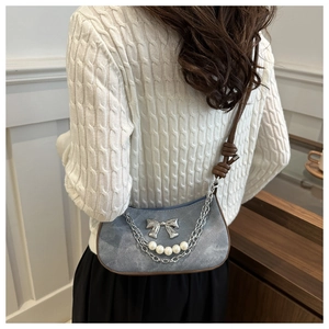 Sac demi-lune en jean avec nœud métallique et chaîne de perles porté par un mannequin