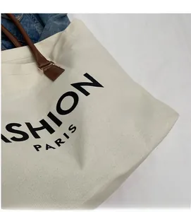 Close-up of cream canvas tote bag with brown leather handles and Fashion Paris print