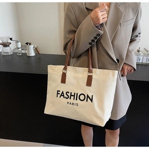 Detailed shot of an off-white canvas tote bag with brown leather handles and Paris print