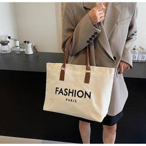 Detail of beige canvas tote bag with brown leather handles and Fashion Paris print