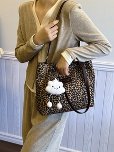 Leopard print tote bag with brown leather handles and a white plush cloud charm on the side