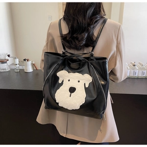 Detail of black tote bag with plush puppy motif on model in a modern cafe setting